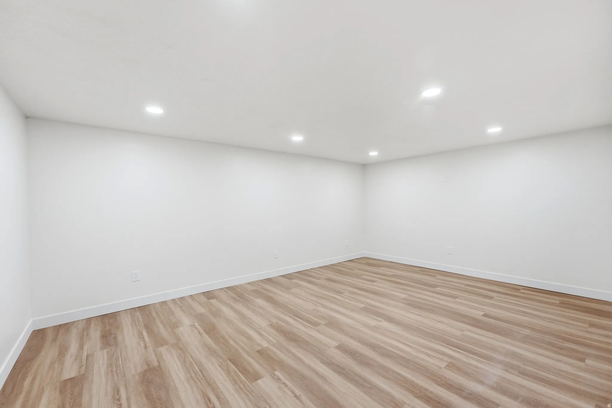 Room with wood-finish flooring, white walls, recessed ceiling lighting, and white baseboards