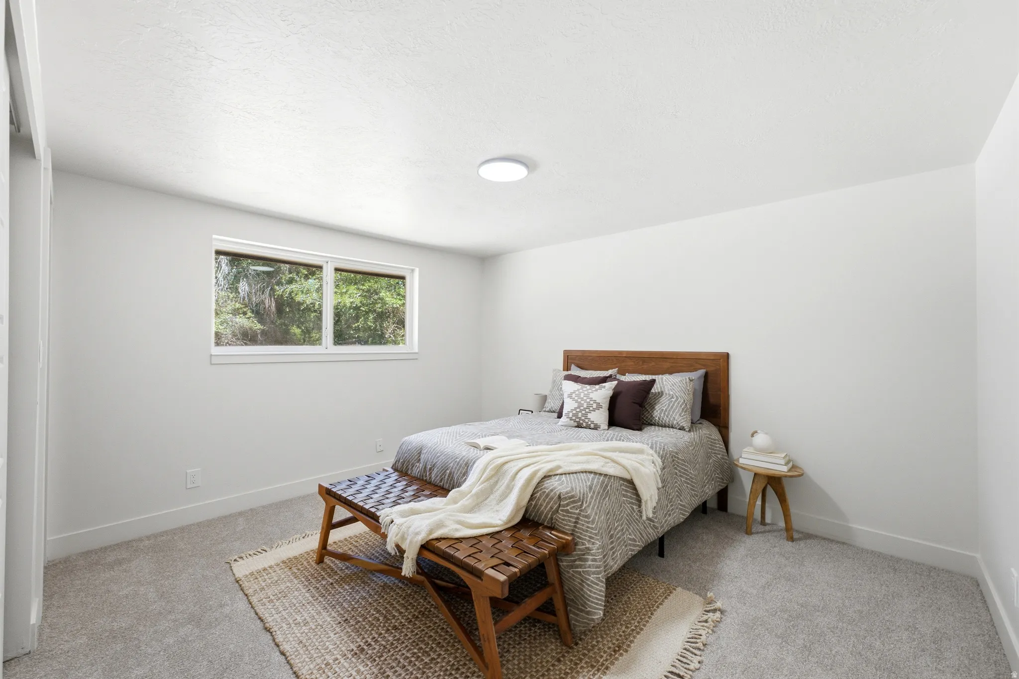 Bedroom featuring light gray carpeting, crisp white walls, a large window, and a flush-mount ceiling light fixture