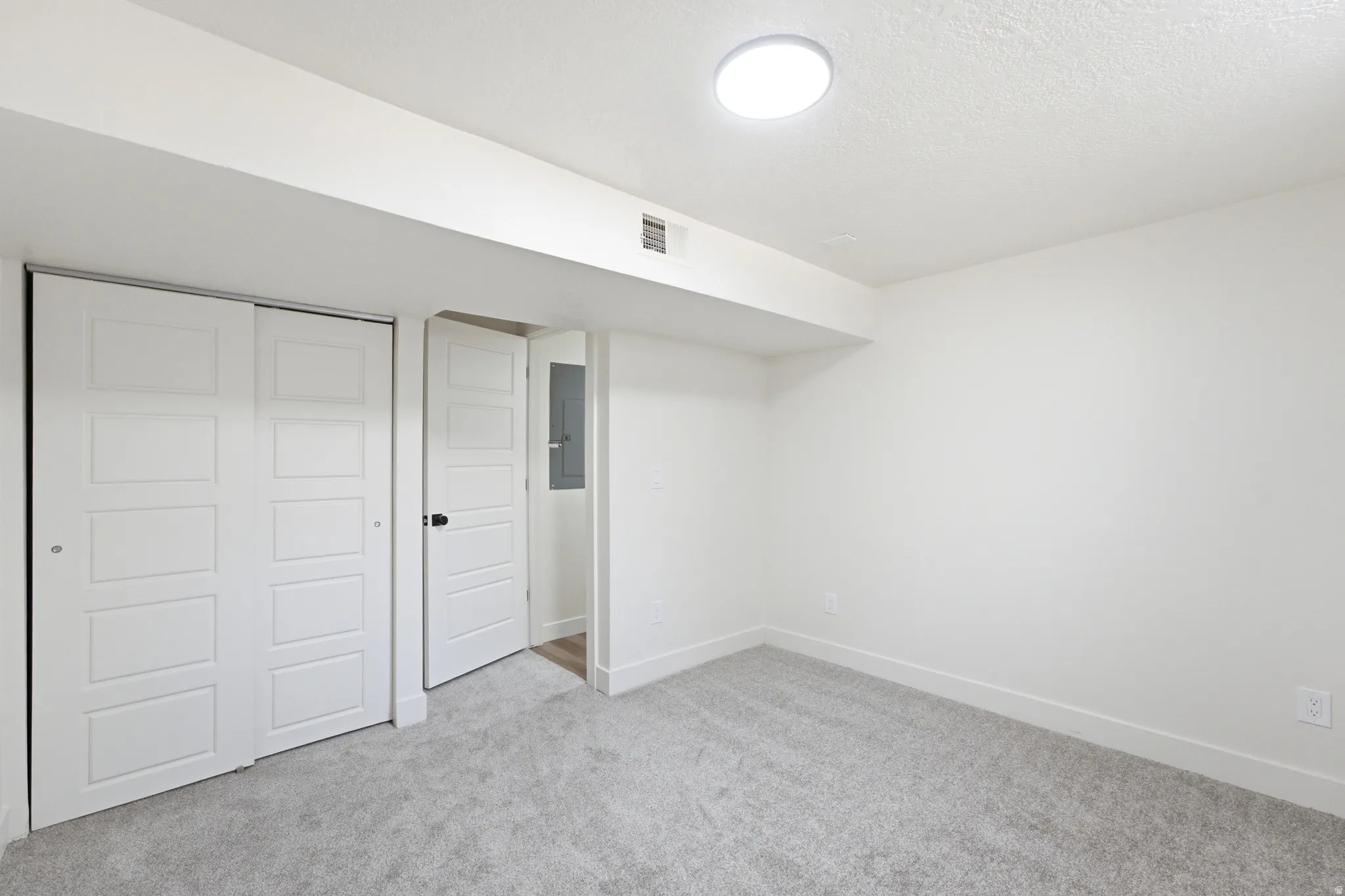 Bright room with light gray carpeting, white walls, and a modern flush-mount ceiling light