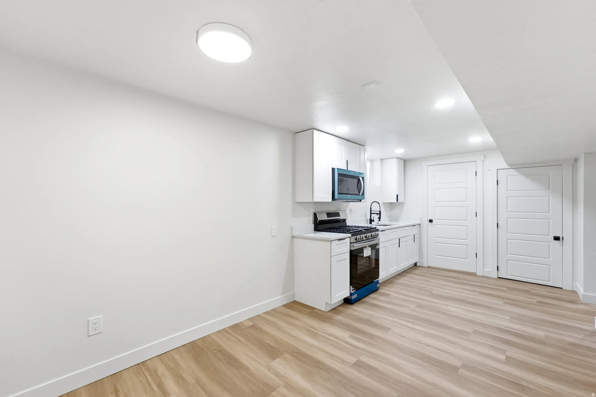 Compact kitchen area featuring white cabinetry, a built-in microwave, a gas range, and a single-basin sink with a gooseneck faucet