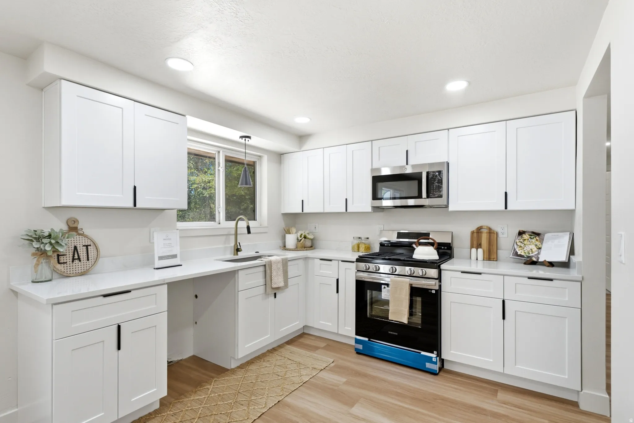Modern kitchen featuring white shaker-style cabinetry with matte black hardware, light-toned countertops, wood-finish flooring, recessed lighting, and a stainless steel appliance suite