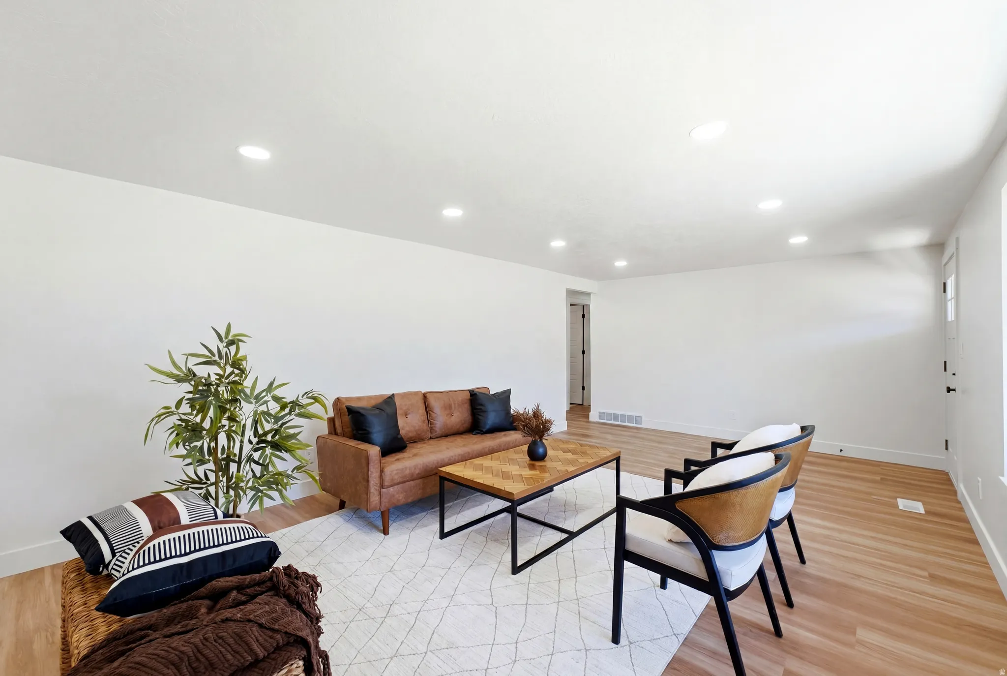 Spacious living area featuring light wood-finish flooring, recessed ceiling lighting, clean white walls, and white baseboards