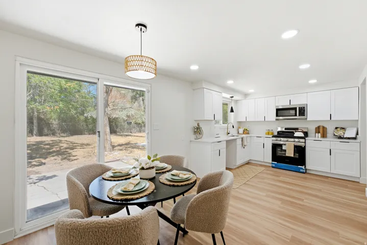 Open-concept kitchen and dining area featuring light wood-finish flooring, white cabinetry, stainless steel appliances, and a sliding glass door