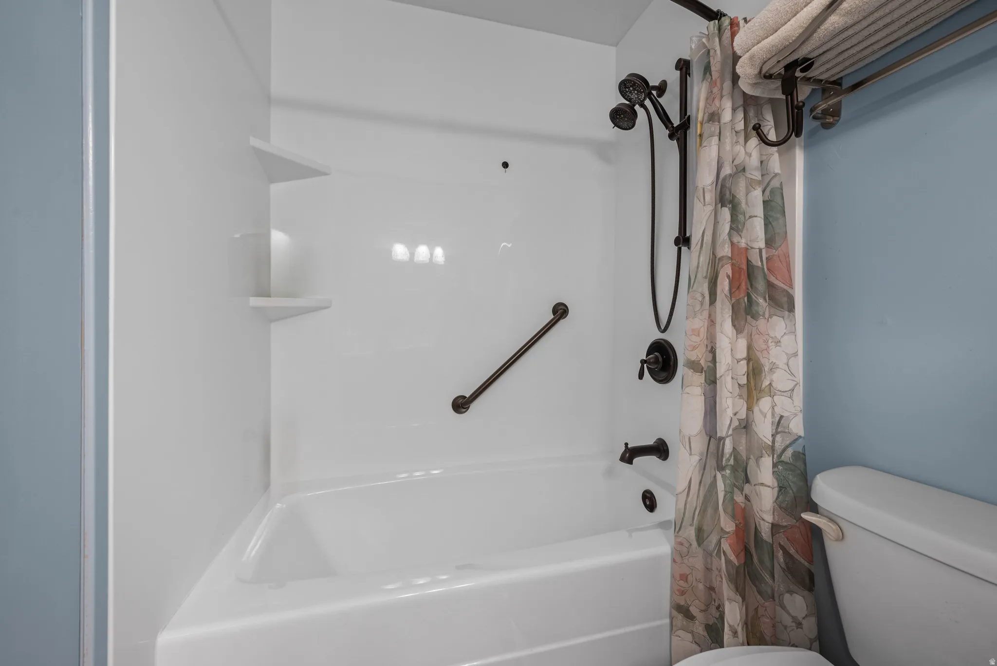 Bathtub and shower combination featuring a white surround, dark bronze fixtures, and a corner grab bar