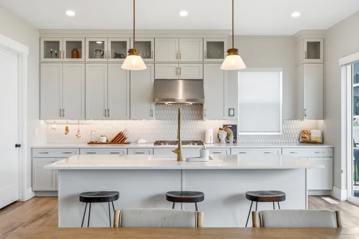 Contemporary kitchen featuring an expansive center island with seating, light gray cabinetry, quartz countertops, a honeycomb tile backsplash, and wood-finish flooring