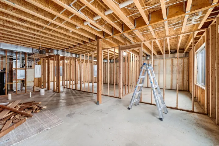 Unfinished basement space with exposed wood framing, concrete flooring, and visible utility conduits