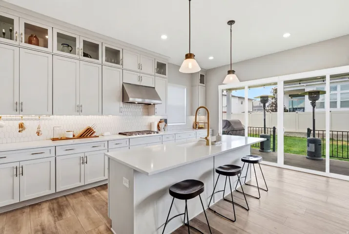 Modern kitchen featuring light-toned cabinetry, a spacious island with seating, pendant lighting, stainless steel appliances, and wood-finish flooring