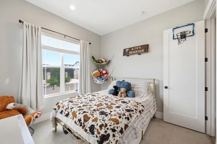 Carpeted room featuring a large window with blinds and drapes, a solid core door with black hardware, and recessed lighting