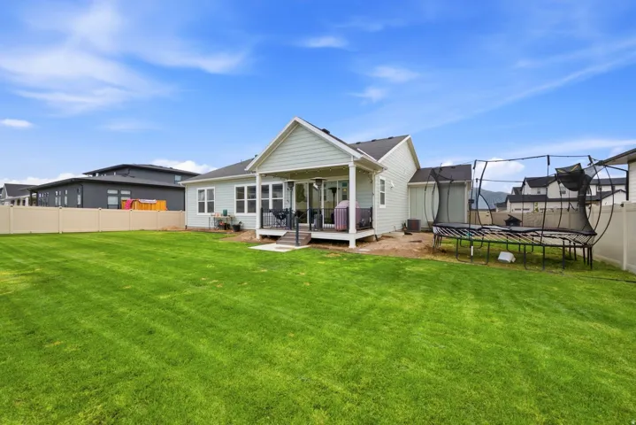 Expansive green lawn with a covered patio, vinyl fencing, and a light-colored exterior facade