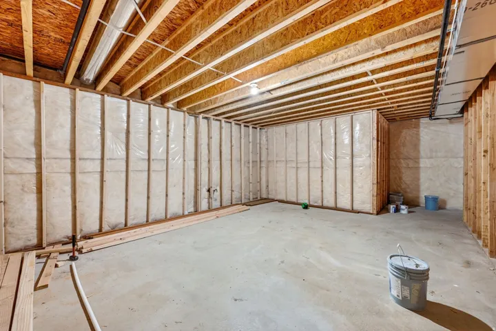 Unfinished lower level featuring exposed wooden ceiling joists, concrete flooring, and framed, insulated walls