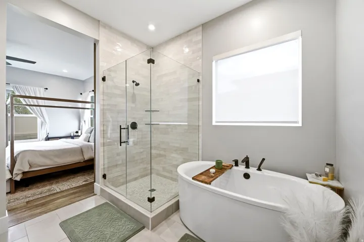 Freestanding soaking tub with matte black fixtures, glass-enclosed shower with subway tile surround, and light tile flooring