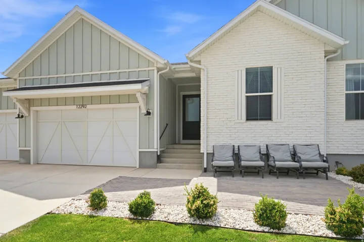 Modern farmhouse-style exterior featuring board and batten siding, painted brick, a two-car garage with decorative hardware, an inviting front entry, and a paver patio