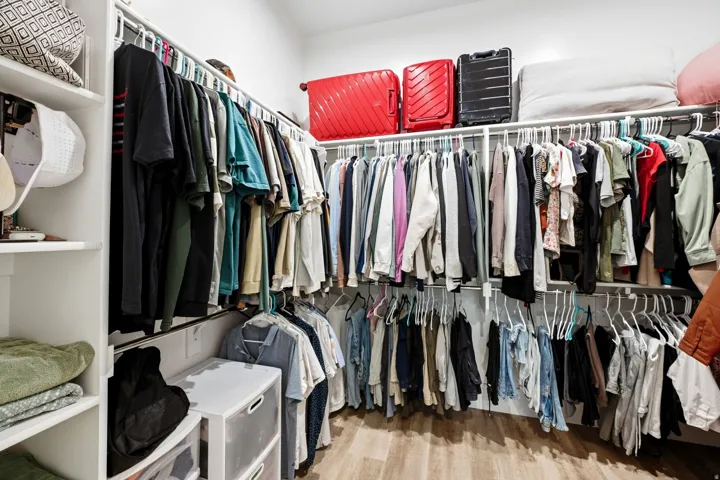Walk-in closet featuring wood-finish flooring, white built-in shelving, white walls, and multiple clothing rods