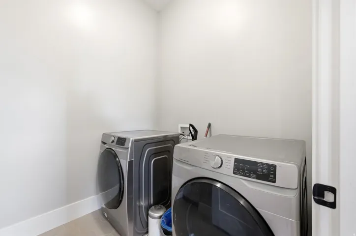 Dedicated laundry area featuring a front-loading washer and dryer, light-toned walls, and a white baseboard