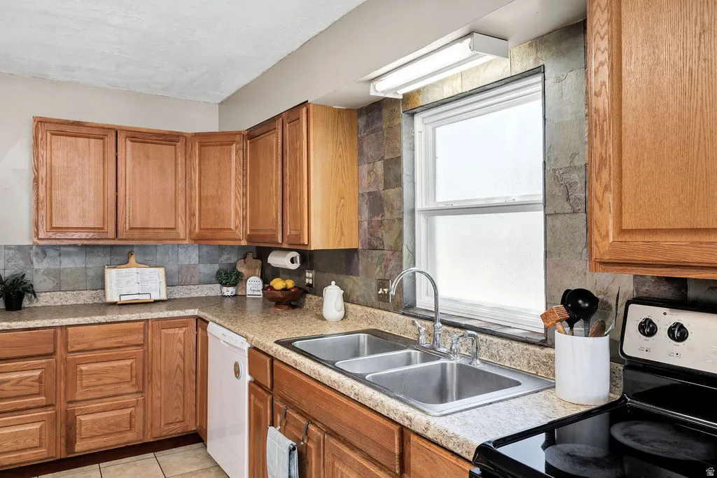 Kitchen featuring wood cabinetry, stone backsplash, dual basin stainless steel sink, and a white dishwasher