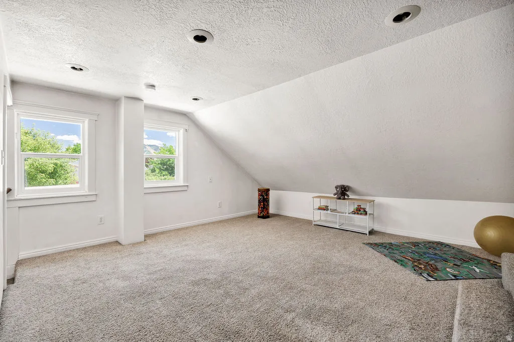Spacious room featuring sloped ceilings, recessed lighting, and soft gray carpeting