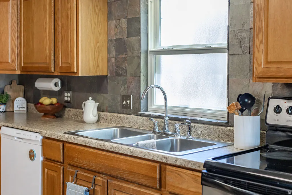 Kitchen featuring wood cabinetry, laminate countertops, stainless steel double basin sink with a high-arc faucet, and slate-style tile backsplash