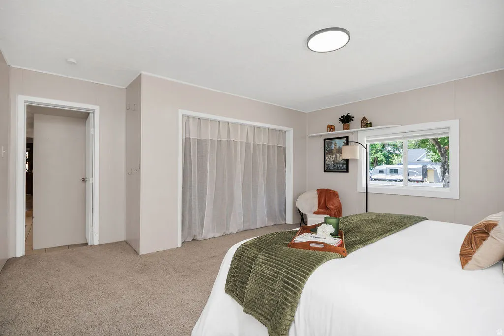 Carpeted bedroom featuring a large window, a flush-mount ceiling light, and a closet with sheer curtains