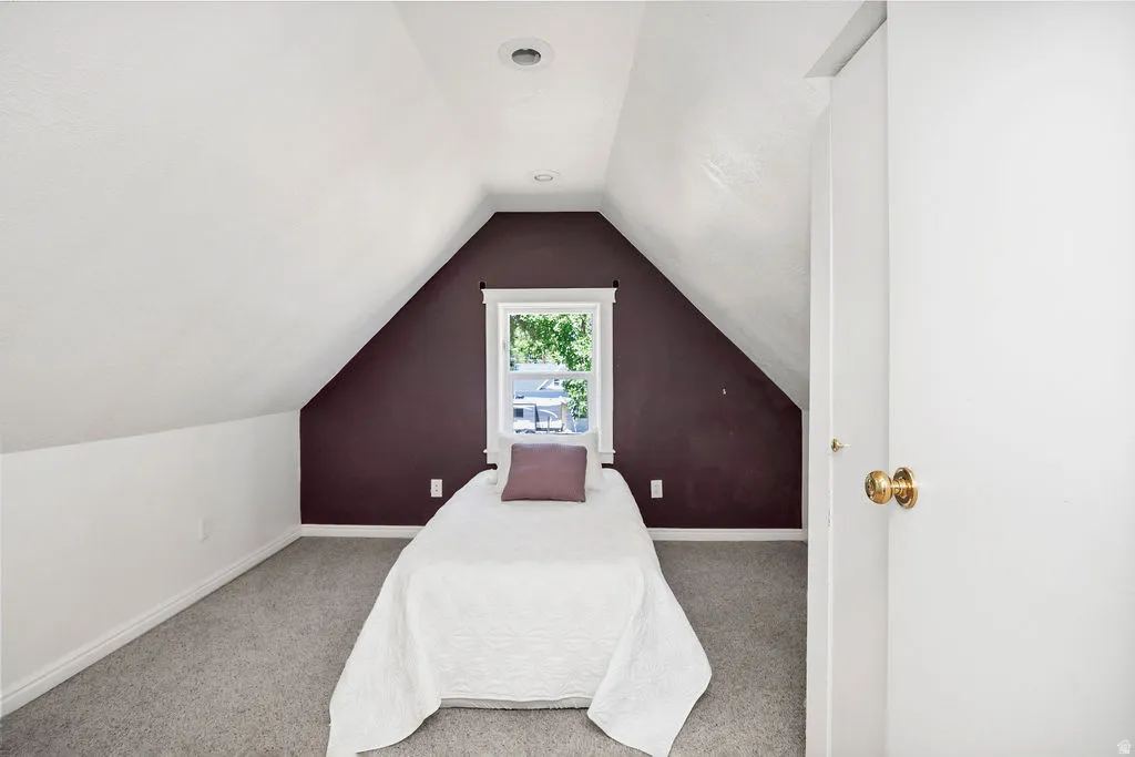 Carpeted room featuring sloped ceilings, a single window, and a white interior door with brass hardware