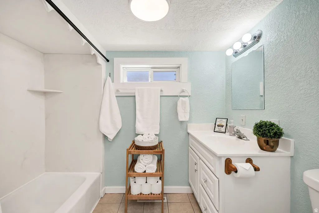 Bathroom featuring a tub/shower combination with a built-in shelf, a window, a single vanity with storage, and tile flooring