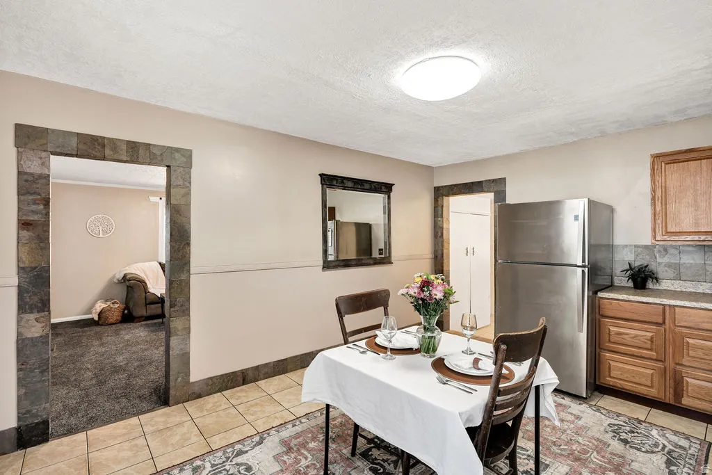 Dining area featuring a tiled floor, stone-trimmed doorway, wood cabinetry, stainless steel refrigerator, and a flush-mount ceiling light fixture