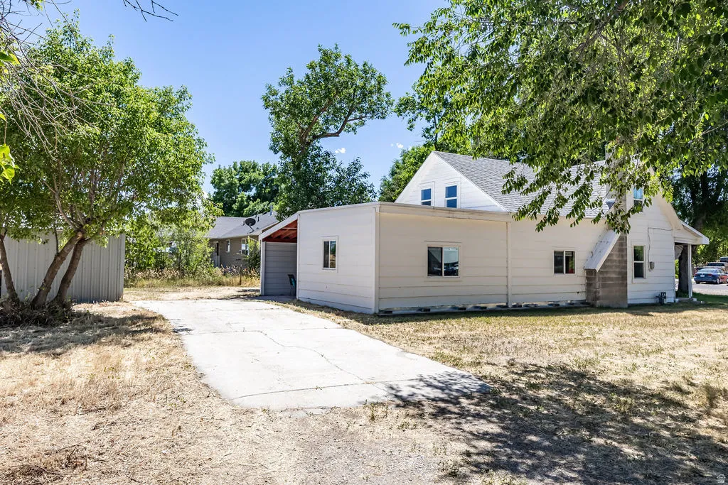 White siding exterior with a pitched shingle roof and concrete parking spaces behind the house