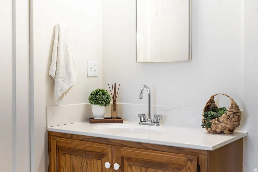 Bathroom vanity featuring a light-toned countertop with integrated sink, chrome faucet, and wood-finish cabinetry with white knobs