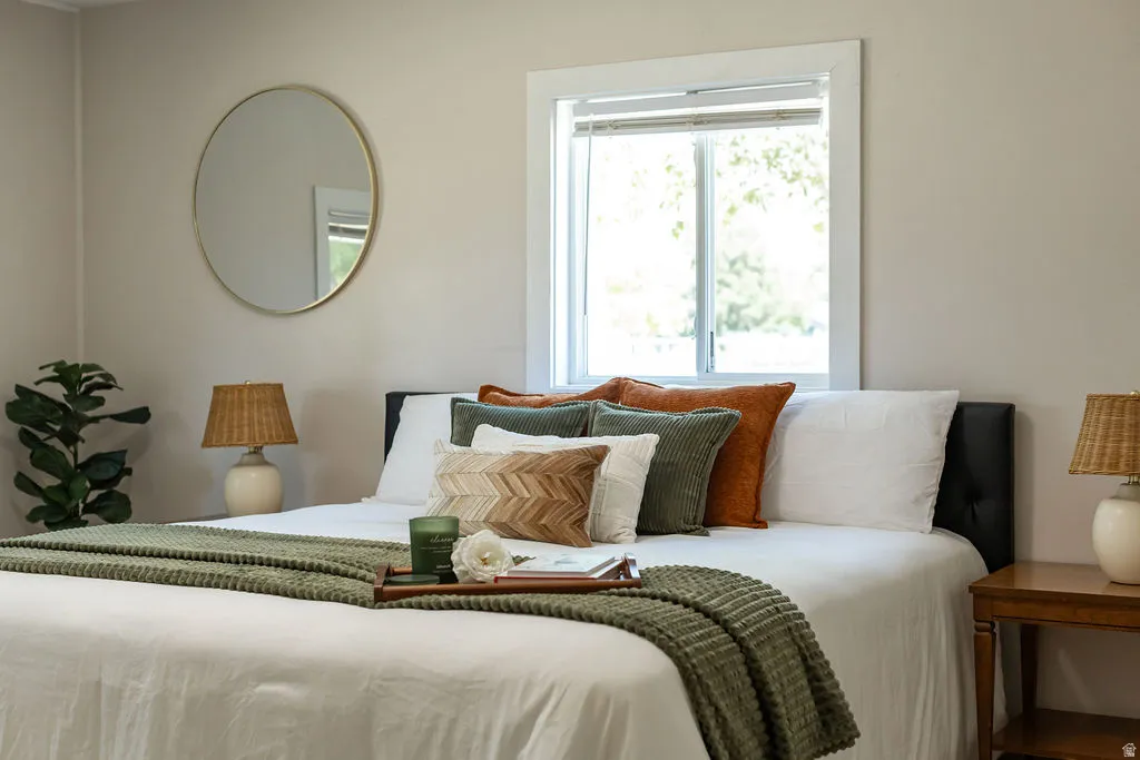 Bedroom featuring a window with white trim, light-toned walls, and a round wall-mounted mirror