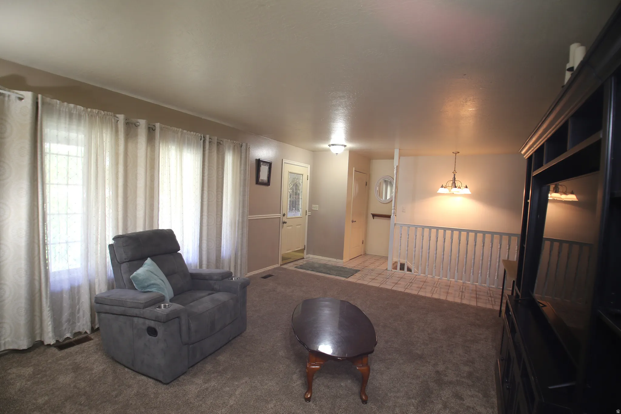 Carpeted living area featuring multiple windows, a decorative front entry door with glass inserts, a tiled entryway, and a white baluster railing