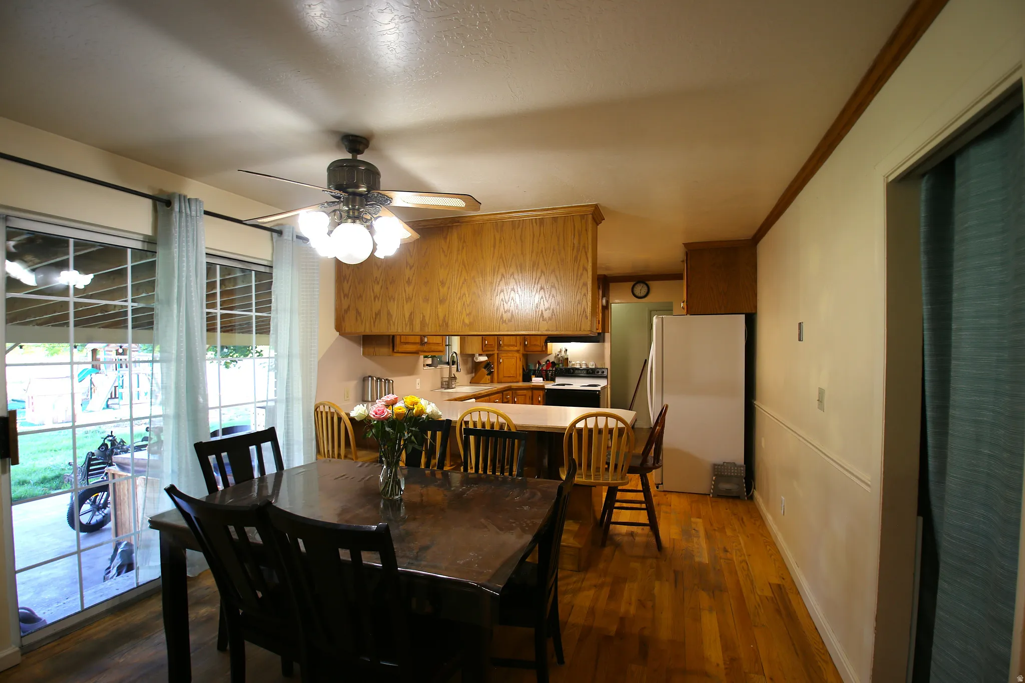 Open-concept dining area featuring wood-finish flooring, a ceiling fan with integrated lighting, and crown molding