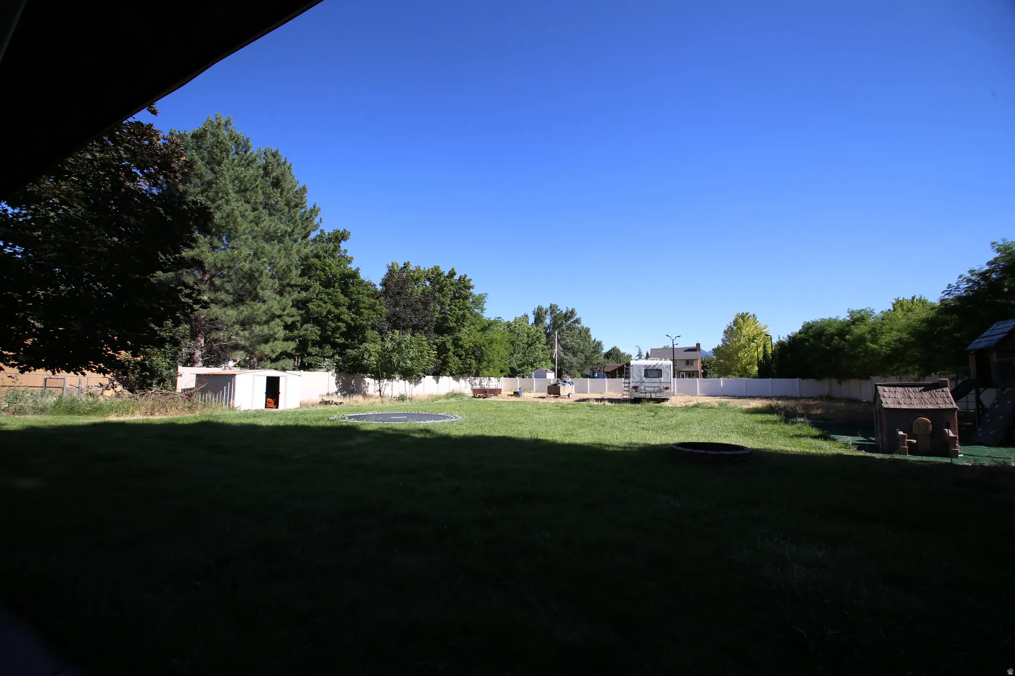Expansive backyard featuring a manicured lawn, perimeter fencing, mature trees, and a storage shed