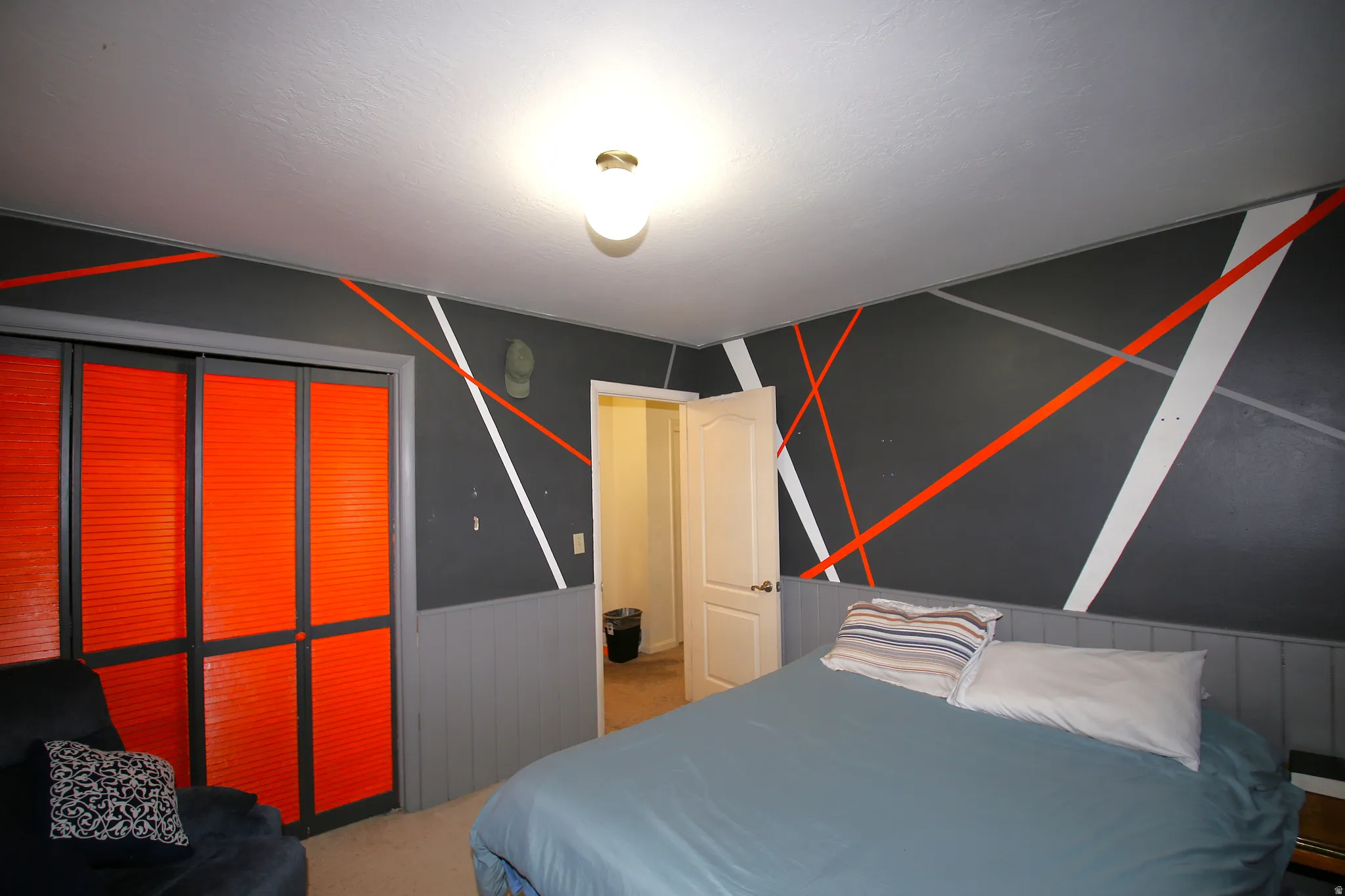 Bedroom featuring a decorative accent wall with geometric stripes, louvered bi-fold closet doors, and painted wainscoting