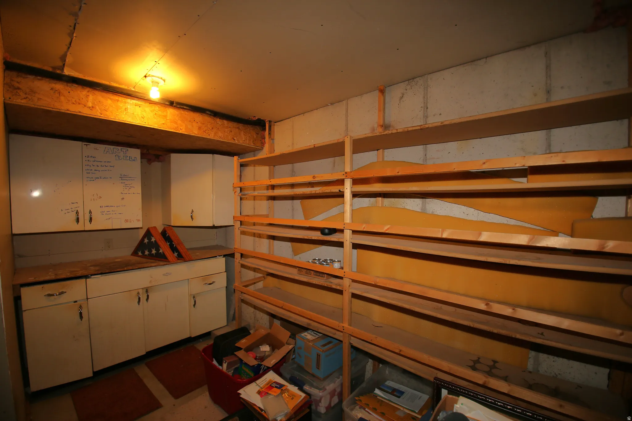 Utility room featuring built-in cabinetry, an overhead light fixture, wood shelving, and exposed concrete walls