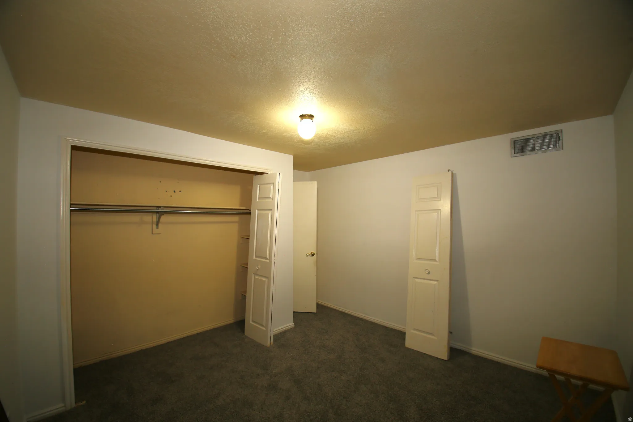 Bedroom featuring a closet with bi-fold doors and a hanging rod, gray carpet flooring, white walls, and a ceiling-mounted light fixture