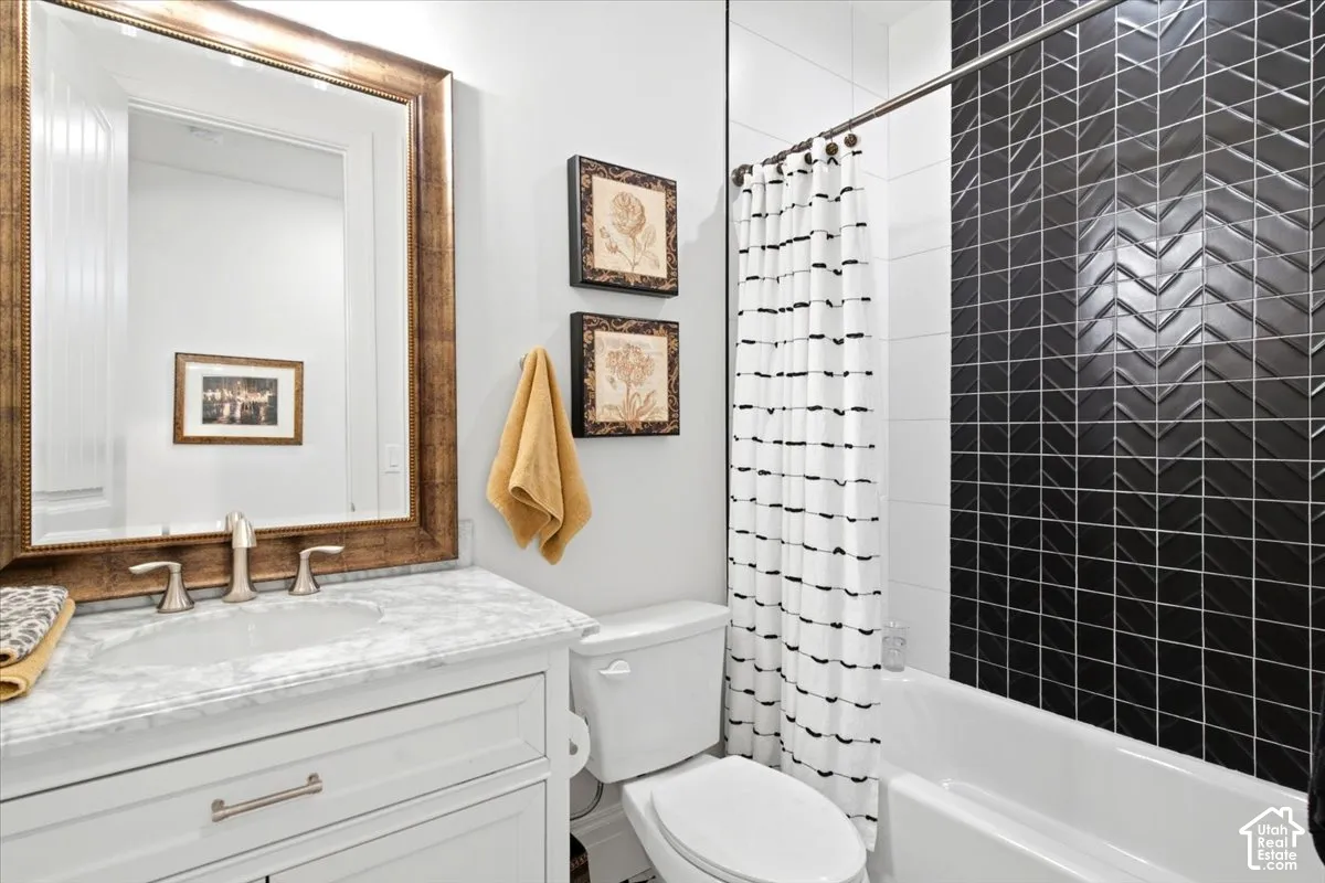 Bathroom featuring a white vanity with an integrated sink and brushed nickel fixtures, a framed mirror, and a white bathtub with a black herringbone tile surround