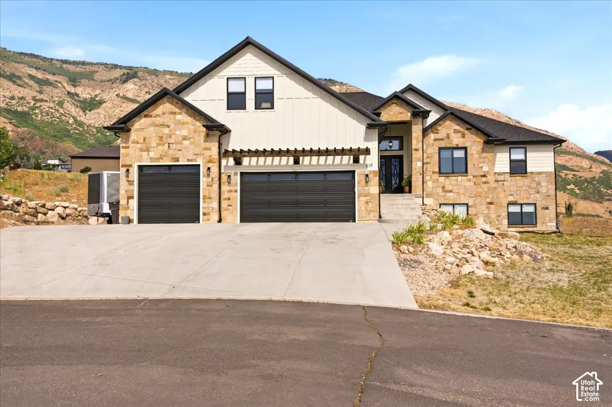 Custom home featuring a stone and vertical siding facade, dark trim, and a prominent two-car garage with modern doors