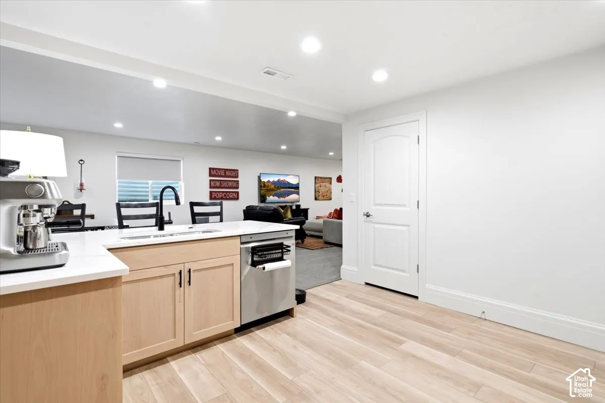 Kitchenette featuring light wood-finish cabinetry, a white countertop, stainless steel sink with a matte black faucet, and a stainless steel dishwasher