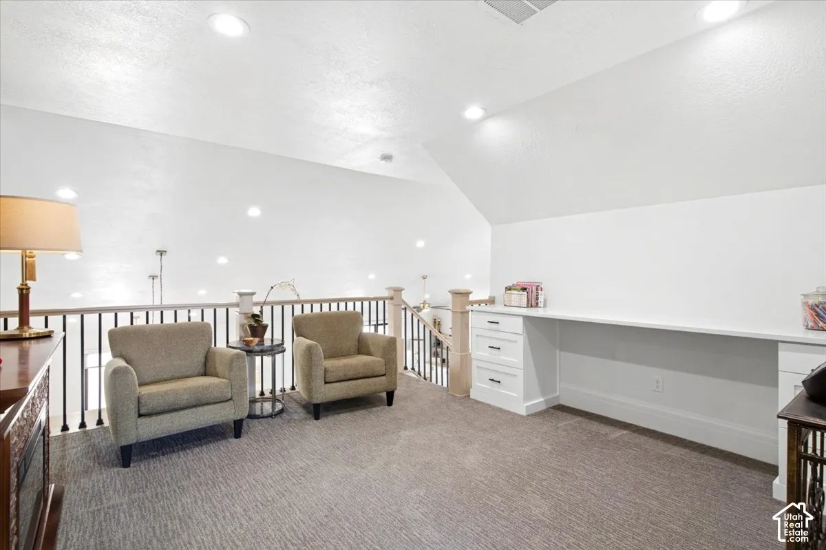 Spacious loft area featuring a built-in white desk with drawers, recessed lighting, and a neutral carpeted floor
