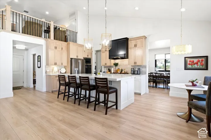 Spacious kitchen featuring light wood-finish flooring, a central island with countertop seating, stainless steel appliances, light-toned cabinetry, and an overhead loft area