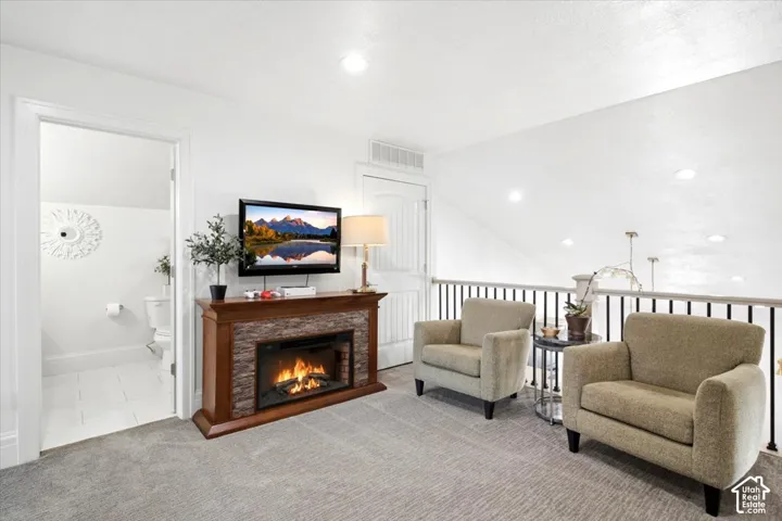 Carpeted loft area featuring a decorative stone-front electric fireplace with a wood-finish mantel, white walls, recessed lighting, and a black iron railing