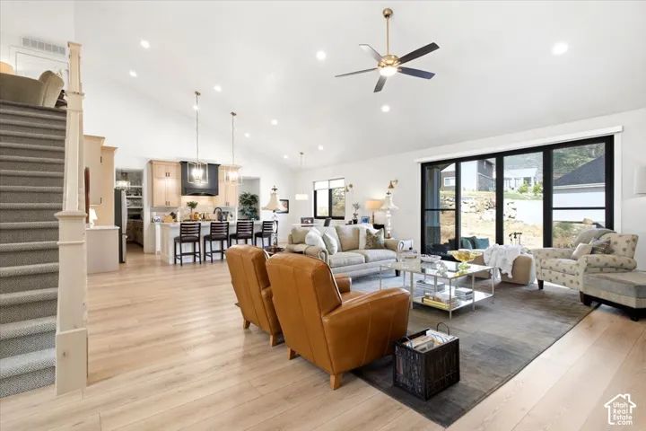 Spacious living area featuring light wood-finish flooring, vaulted ceilings with recessed lighting, and a modern ceiling fan