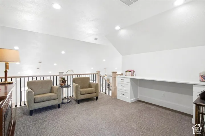 Spacious loft area featuring a built-in white desk with drawers, recessed lighting, and a neutral carpeted floor