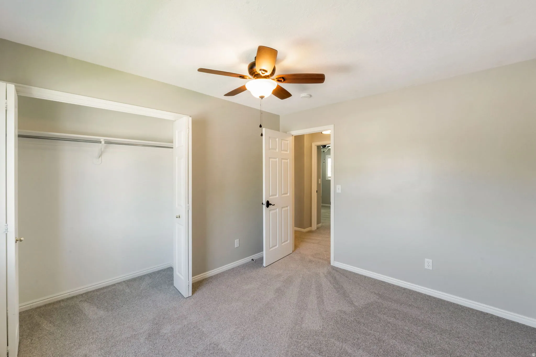 Carpeted interior room featuring light gray walls, white trim, and a ceiling fan with light fixture