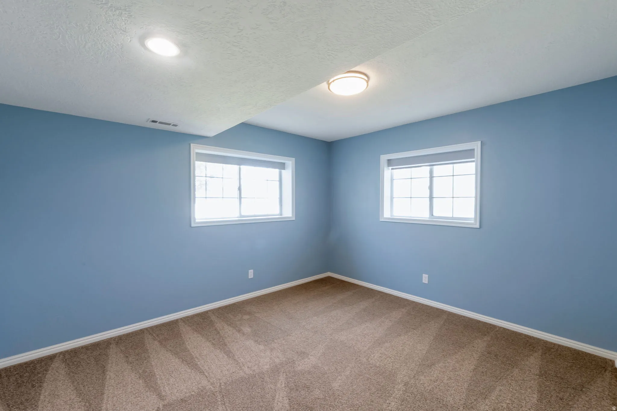 Room featuring two windows with white trim, light blue walls, and patterned carpeting
