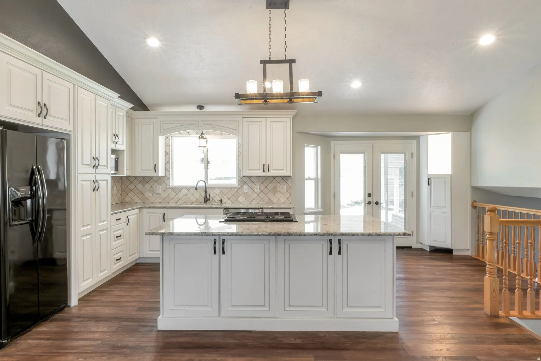 Spacious kitchen featuring white cabinetry, a large kitchen island with a built-in cooktop, granite countertops, and wood-finish flooring
