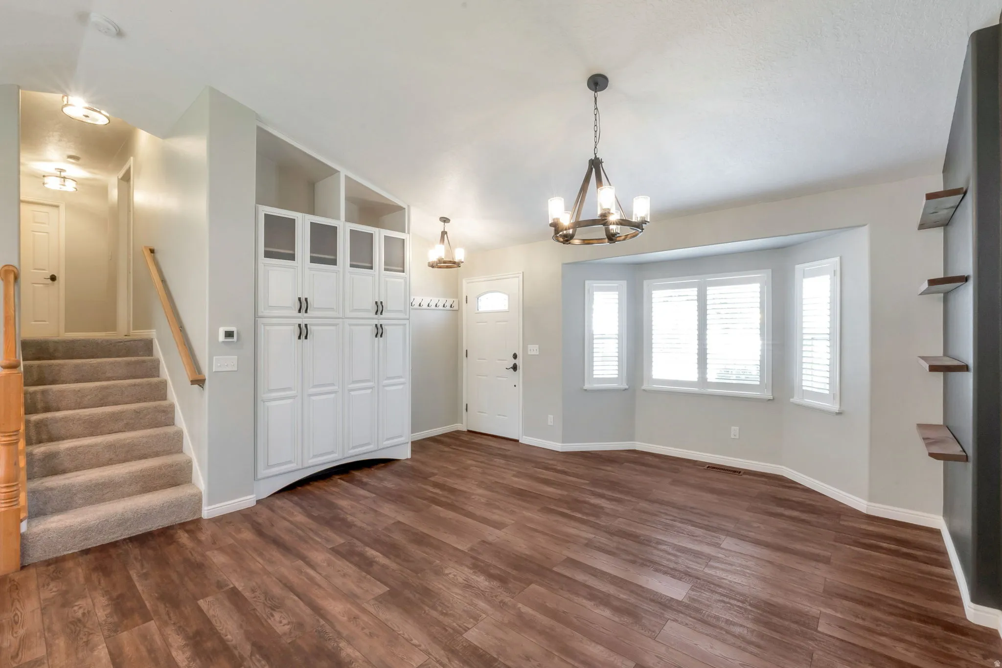 Open living area featuring wood-finish flooring, a contemporary chandelier, and a bay window with white plantation shutters