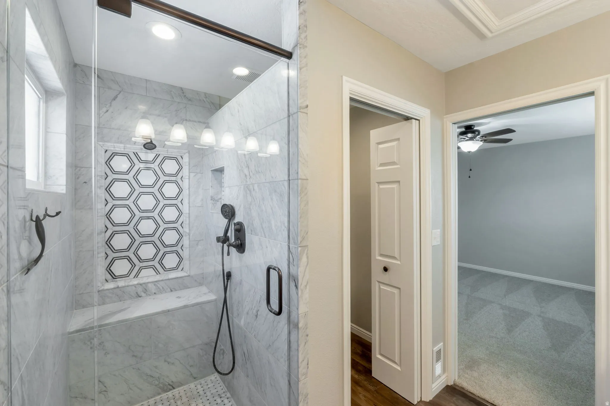 Spacious shower featuring white marble-look tiling, a built-in bench, and a decorative hexagonal accent tile