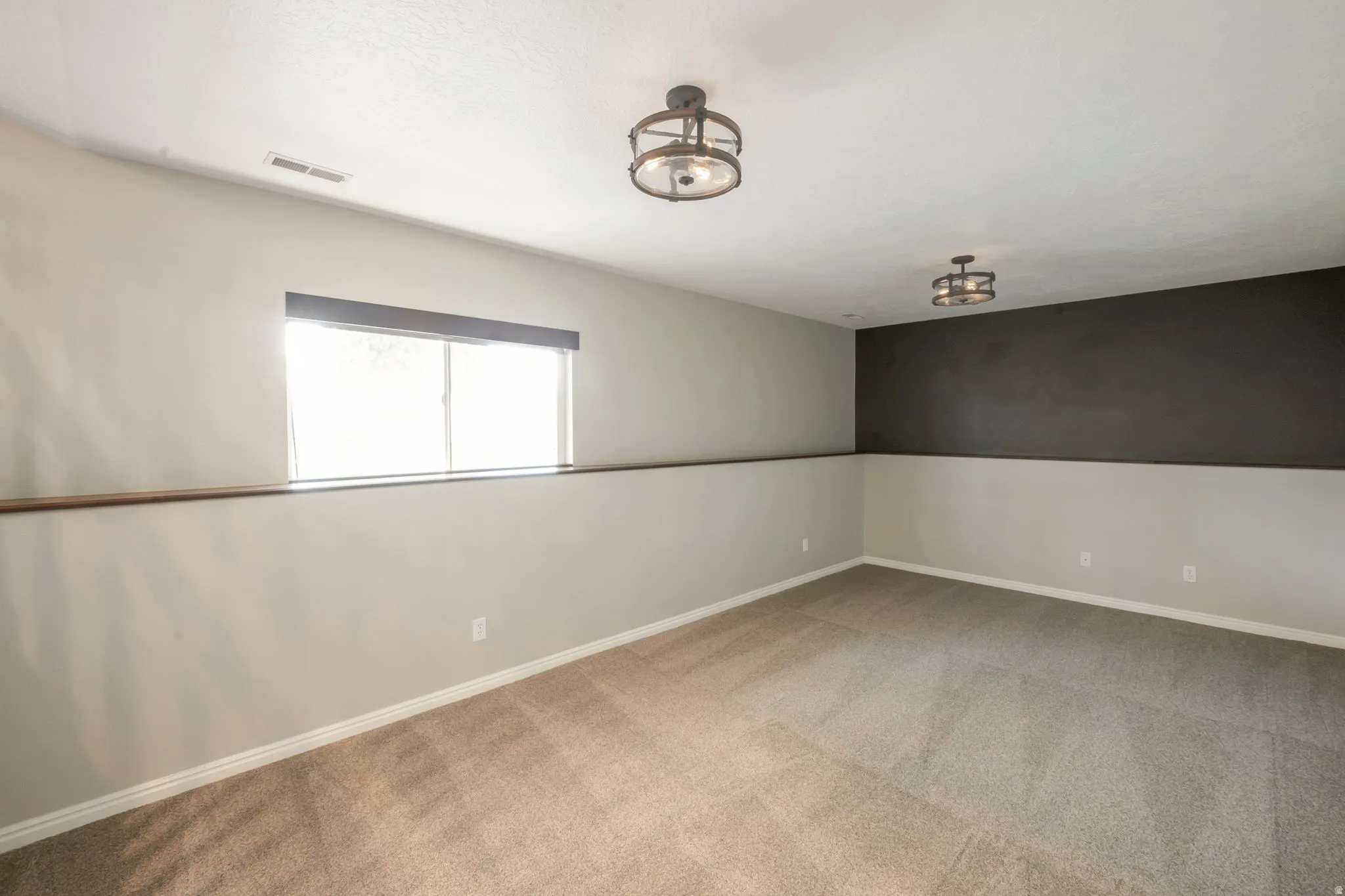 Spacious room featuring neutral carpet flooring, a broad window, and two flush-mount light fixtures
