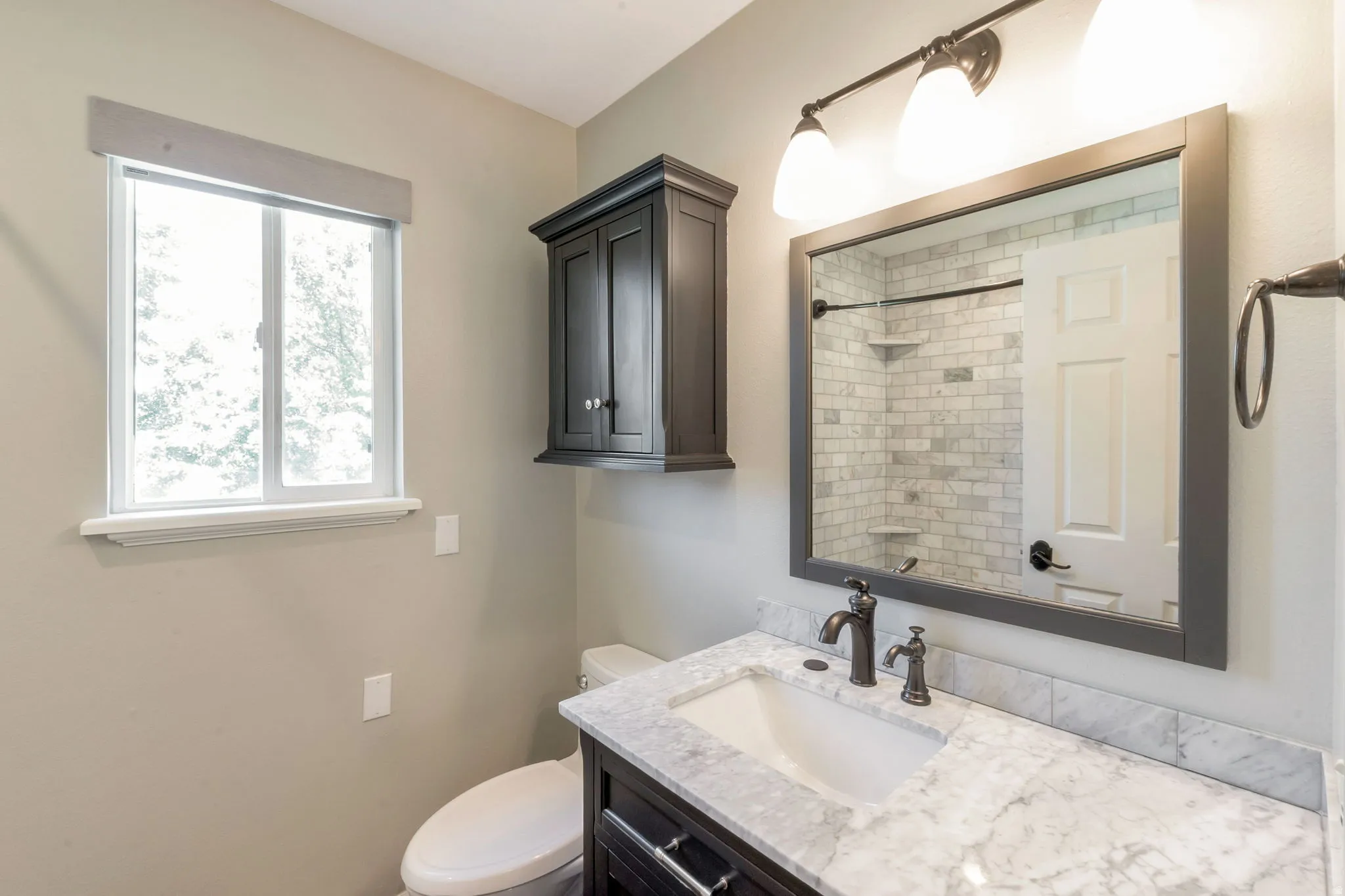 Bathroom featuring a vanity with a white countertop, dark wood-finish cabinetry, and a rectangular mirror with integrated lighting