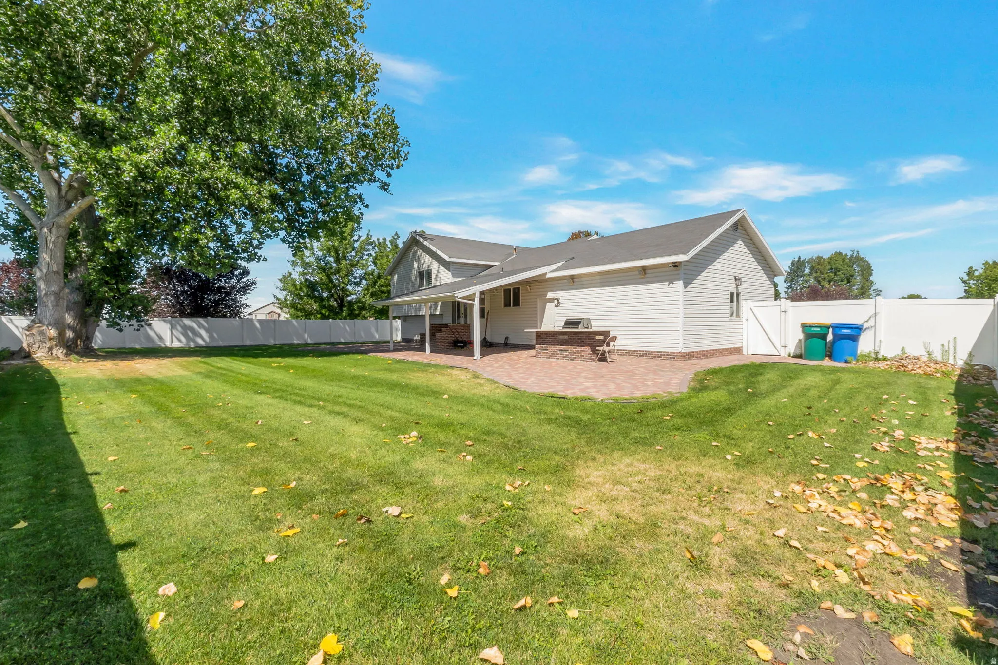 Expansive backyard featuring a manicured lawn, mature shade tree, and white privacy fencing